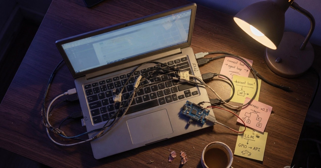 Developer desk with laptop, cables, and a microcontroller suggesting an agent tool harness